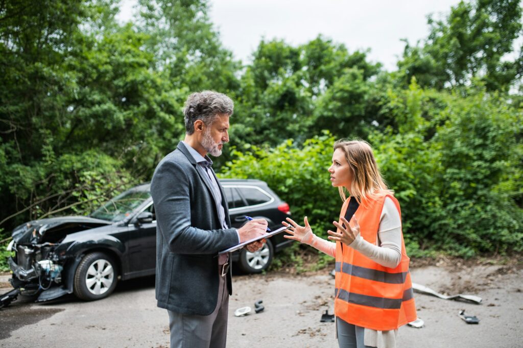 An insurance agent talking to a woman driver by the car on the road after an accident.